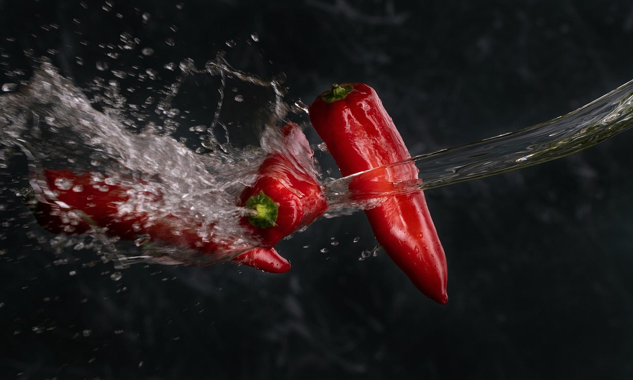Red peppers being rinsed with water against a dark background